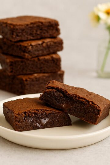 Stack of fudgy brownies with gooey chocolate centers on a white plate.