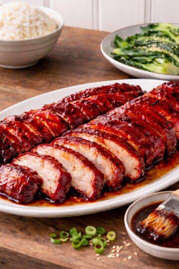 sliced char sui on a platter, bowl of rice and sauteed bok choy on wood countetop