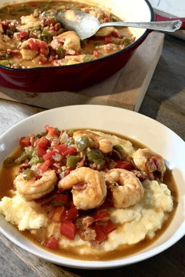 shrimp and stone ground white grits in a bowl on a wood countertop, cast iorn pan of shrimp souace in the background