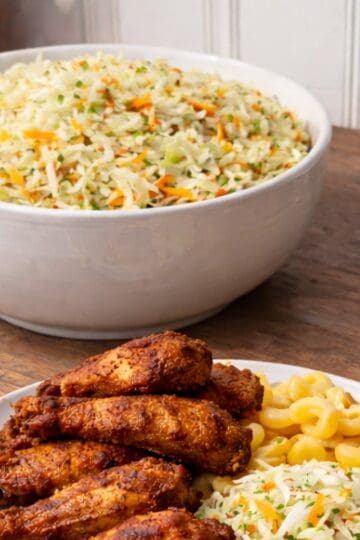 Large bowl of American vinegar coleslaw made with shredded cabbage and carrots, styled on a wooden kitchen counter.