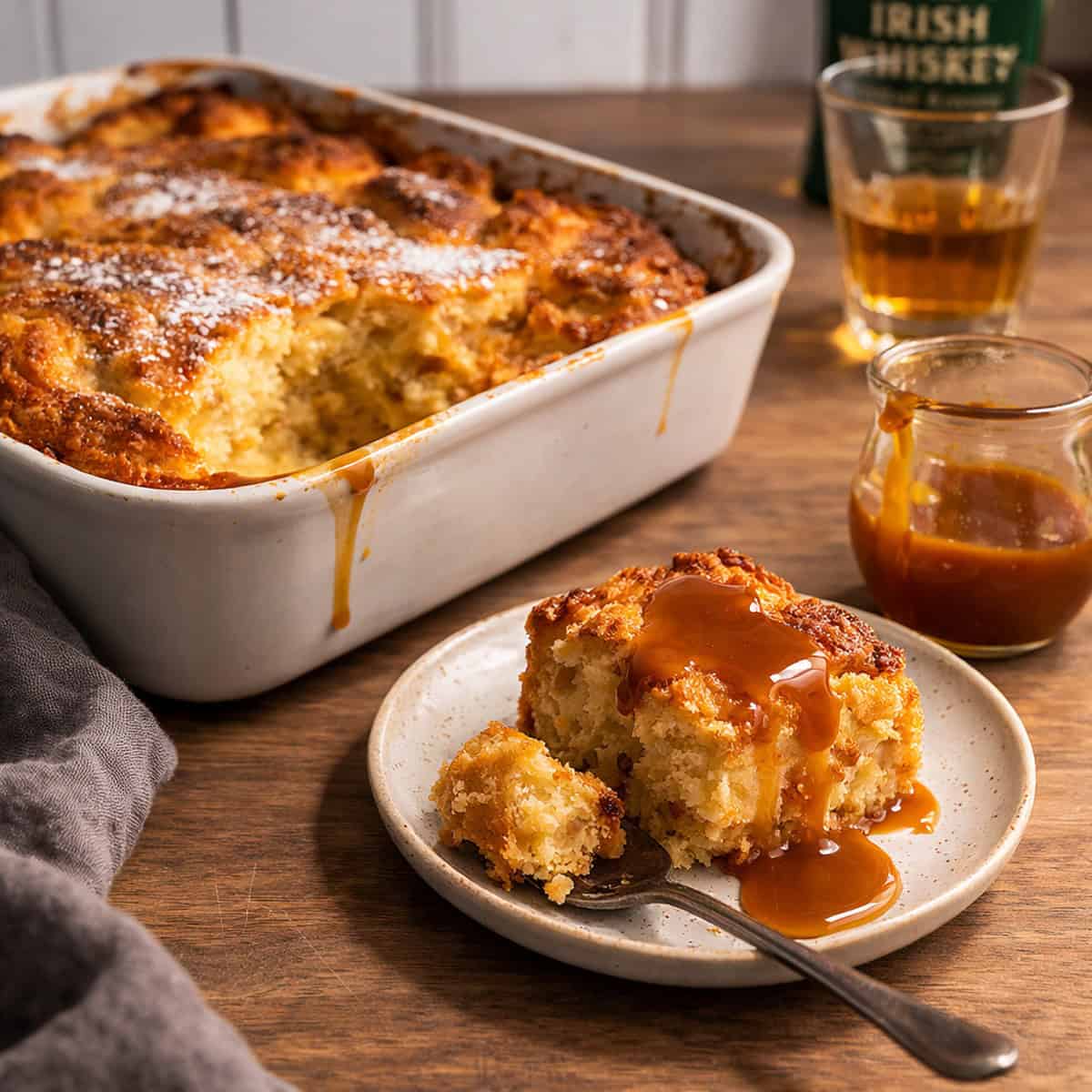 irish bread pudding in a cassarole dish, single serving on a msall plate on a wood countertop